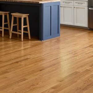 Kitchen scene featuring warm hardwood floors, a blue island with two wooden stools, white cabinets, and a stainless steel refrigerator.